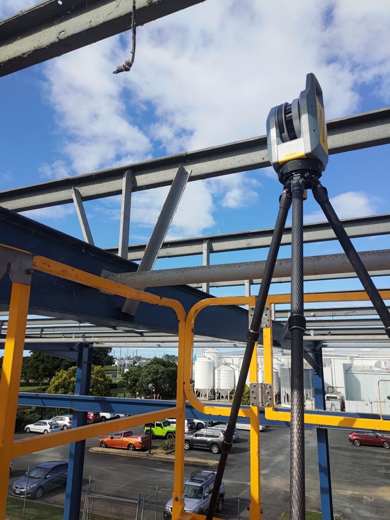Trimble X7 laser scanner on a tripod among steel roof beams on an elevated platform with yellow handrails