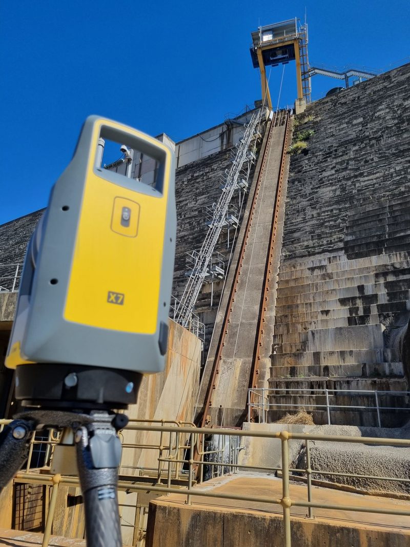 Close-up of the Trimble X7 laser scanner in front of a large concrete structure with a steel access stairway